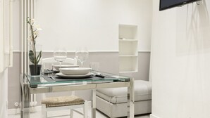 Uma sala de jantar moderna com uma mesa de vidro, cadeiras brancas e uma orquídea em vaso.