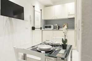 A modern kitchen with white cabinets, a microwave, and a small dining area with a glass table and chairs.