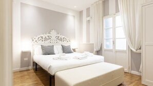 Quarto de hotel com uma cama grande, cabeceira branca e piso de madeira.