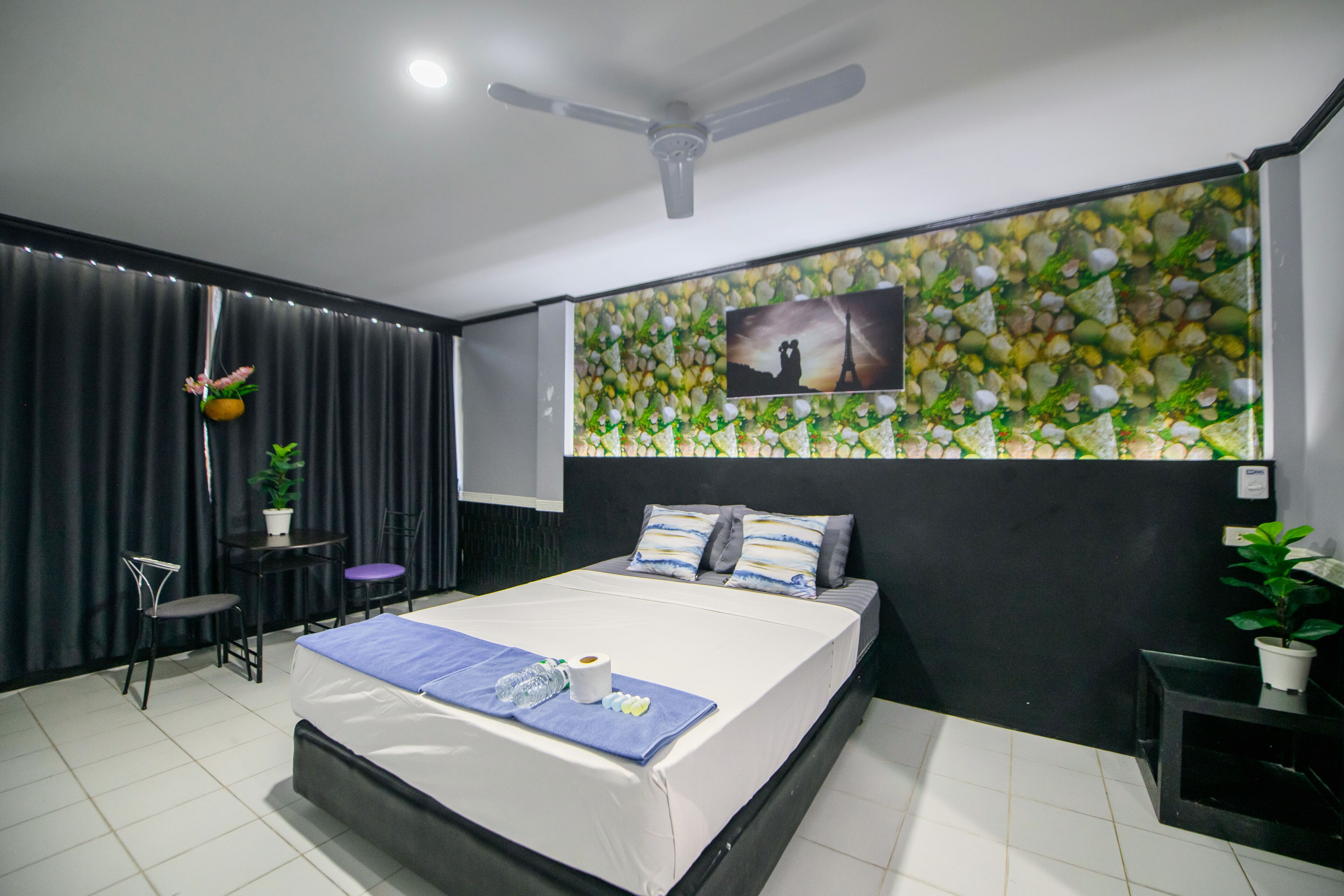 A modern hotel room with a large bed, a ceiling fan, a wall-mounted TV, and a decorative wall with a green and white pattern.