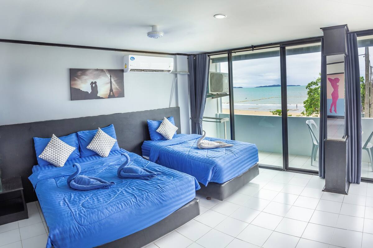 A hotel room with two beds, a balcony with a view of the beach, and an air conditioning unit on the wall.