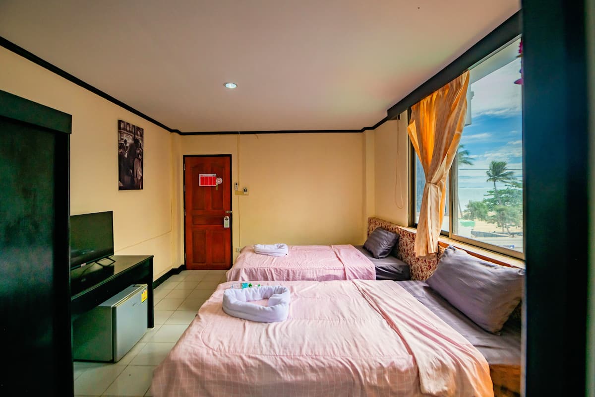A hotel room with two beds, a TV, a small desk, and a window with curtains.