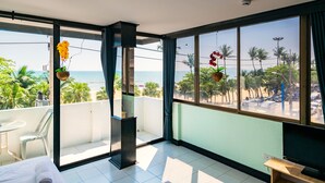A room with a balcony overlooking a beach, a bed, a TV, and a small table. - Happy Jomtien - Direct Beach Access, Sea View & Central Location (Pattaya)