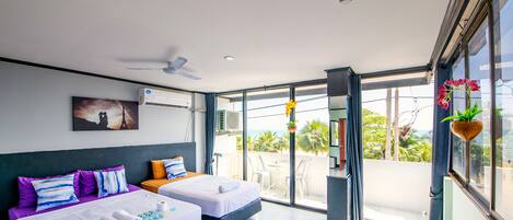 A hotel room with two beds, a ceiling fan, an air conditioning unit, a balcony with a view of the sea, and a hanging plant.