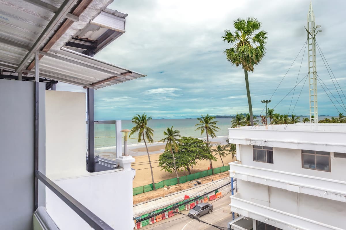 A view from a balcony overlooking a beach with palm trees, a sandy shore, and a clear sky.