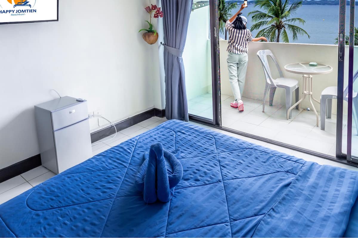 A hotel room with a large bed, a desk, a chair, and a balcony with a view of the sea.
