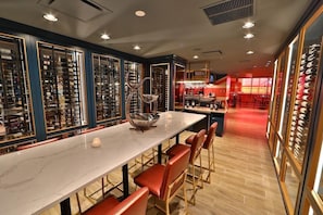 Een bar met een lange toonbank, rode gestoffeerde stoelen en wijnrekken op de achtergrond.