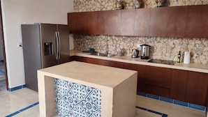 A modern kitchen with a central island, a stone backsplash, wooden cabinets, and a stainless steel refrigerator. - Casa Azulí Santiago  (Mérida)