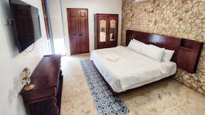 A bedroom with a bed, a wooden dresser, a mirror, a ceiling fan, and a stone wall. - Casa Azulí Santiago  (Mérida)