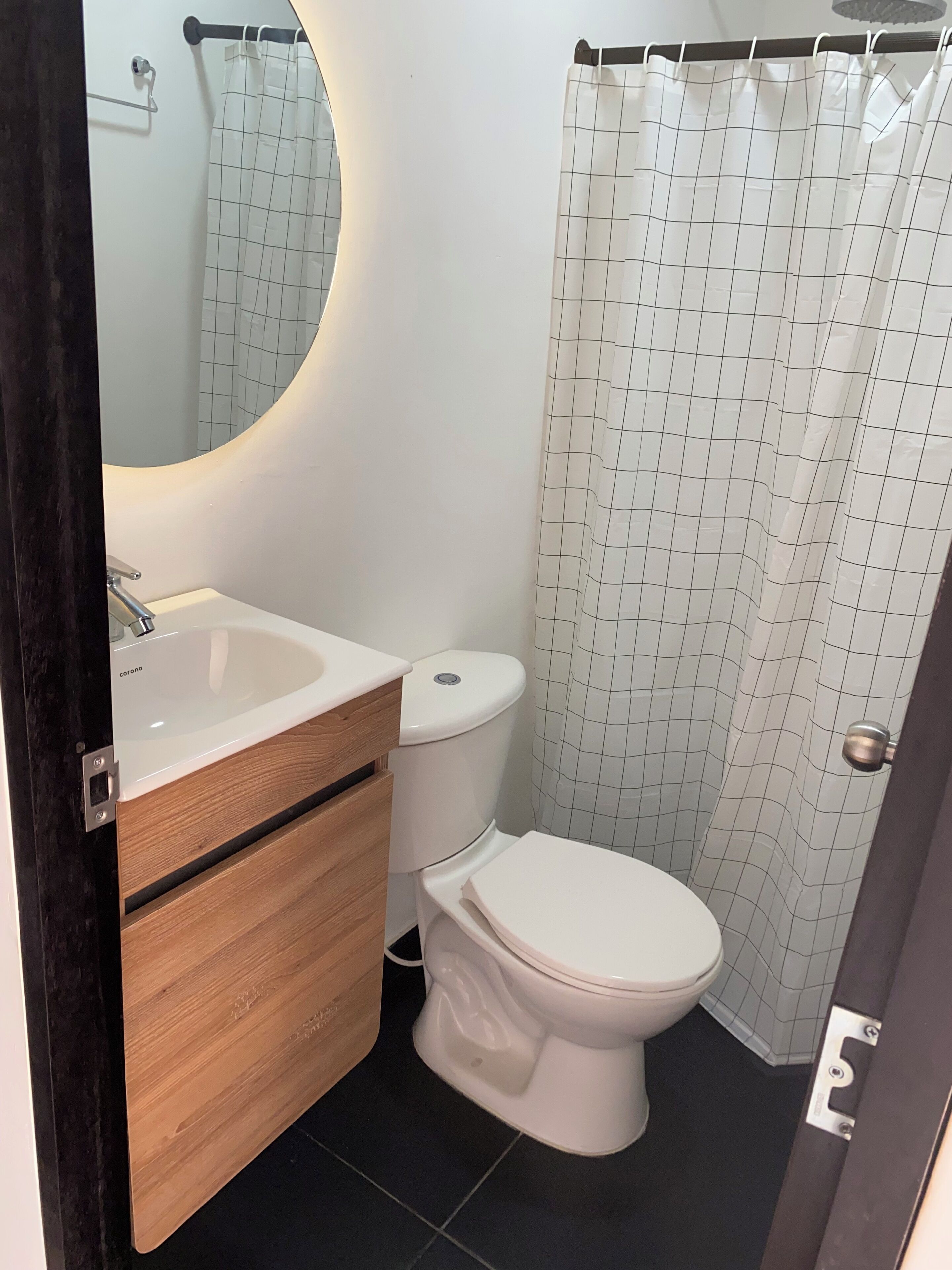 A bathroom with a white sink, wooden vanity, white toilet, and a shower curtain with a grid pattern.