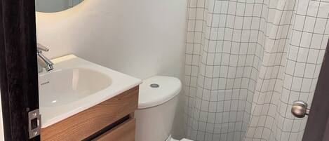A bathroom with a white sink, wooden vanity, white toilet, and a shower curtain with a grid pattern.