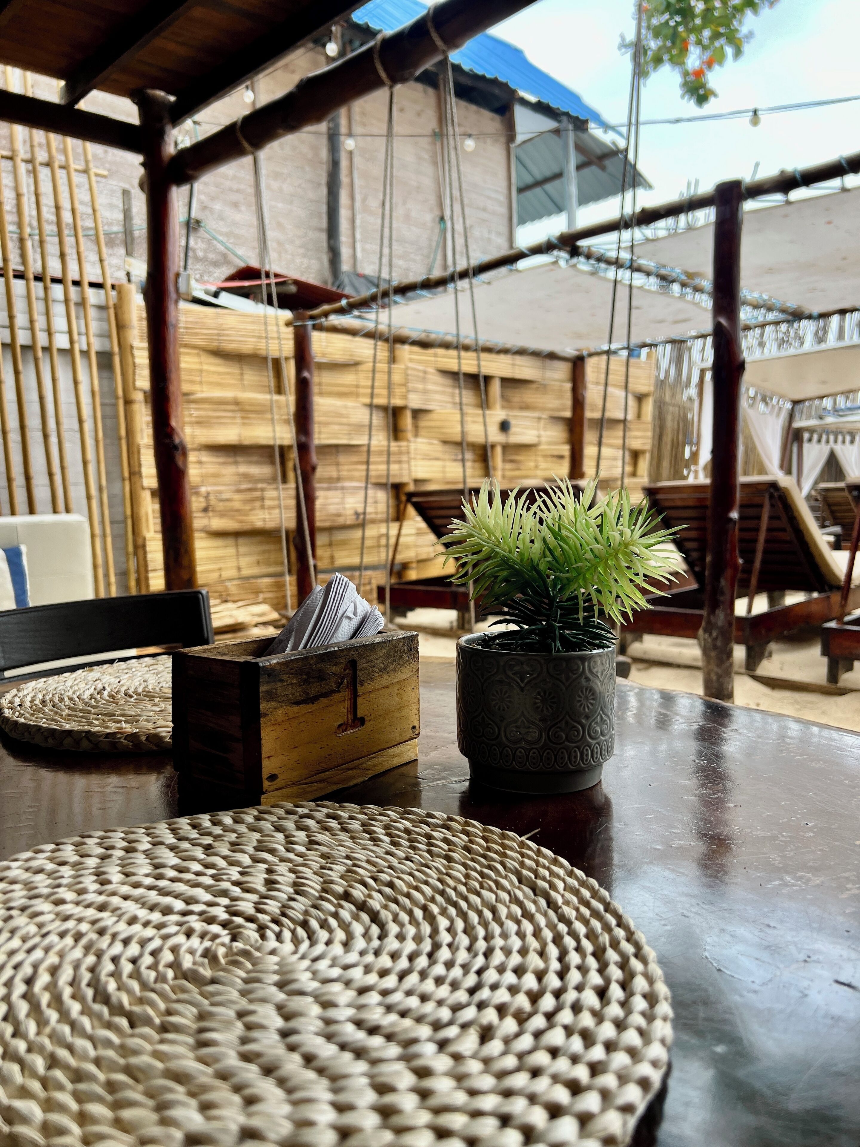 Un espace extérieur aménagé dans un style rustique, avec des tapis en fibres naturelles, une table en bois et une plante en pot.