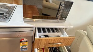 A kitchen with a microwave, a stove, and a drawer with kitchen utensils.