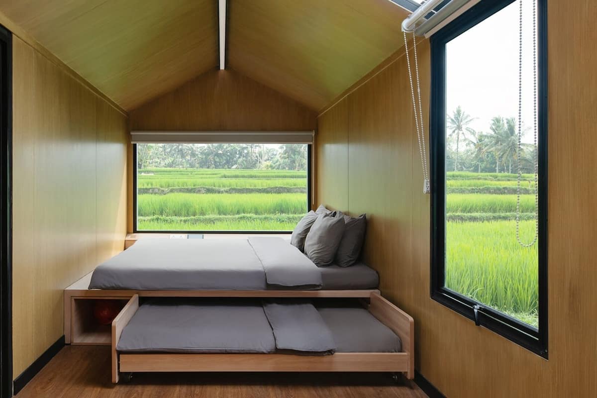 Una habitación pequeña con cama, ventana y vista a un campo verde.
