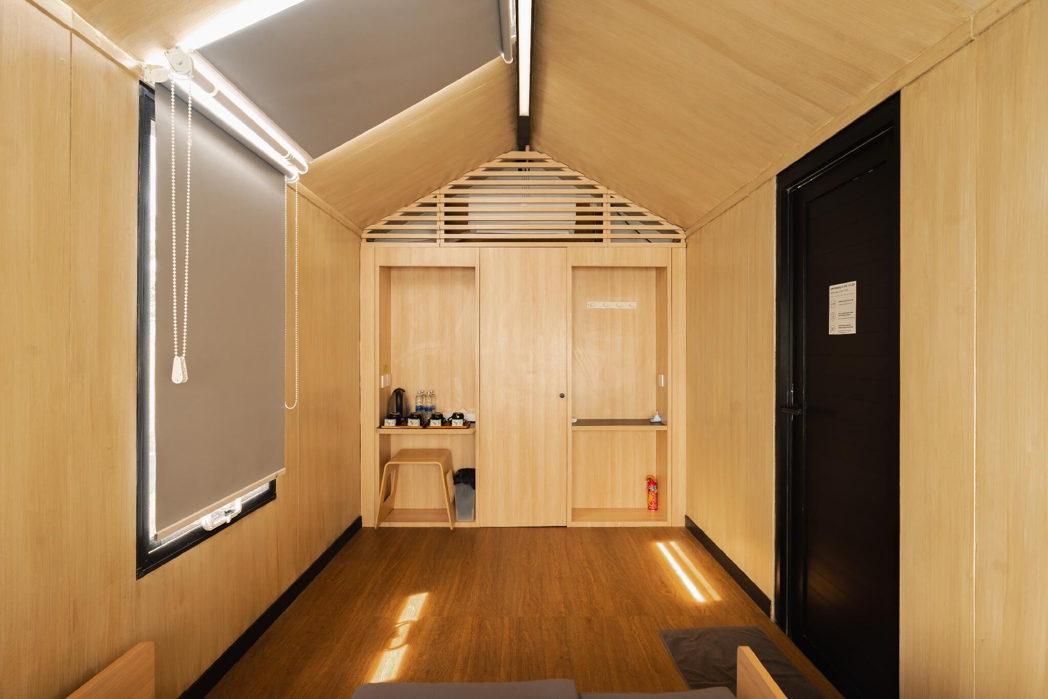 Een hal met houten wanden en plafond, een zwarte deur, en een zithoekje met een tafel en stoelen.