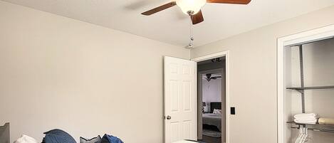 Ein Schlafzimmer mit Bett, Deckenventilator, weißer Tür und Kleiderschrank.