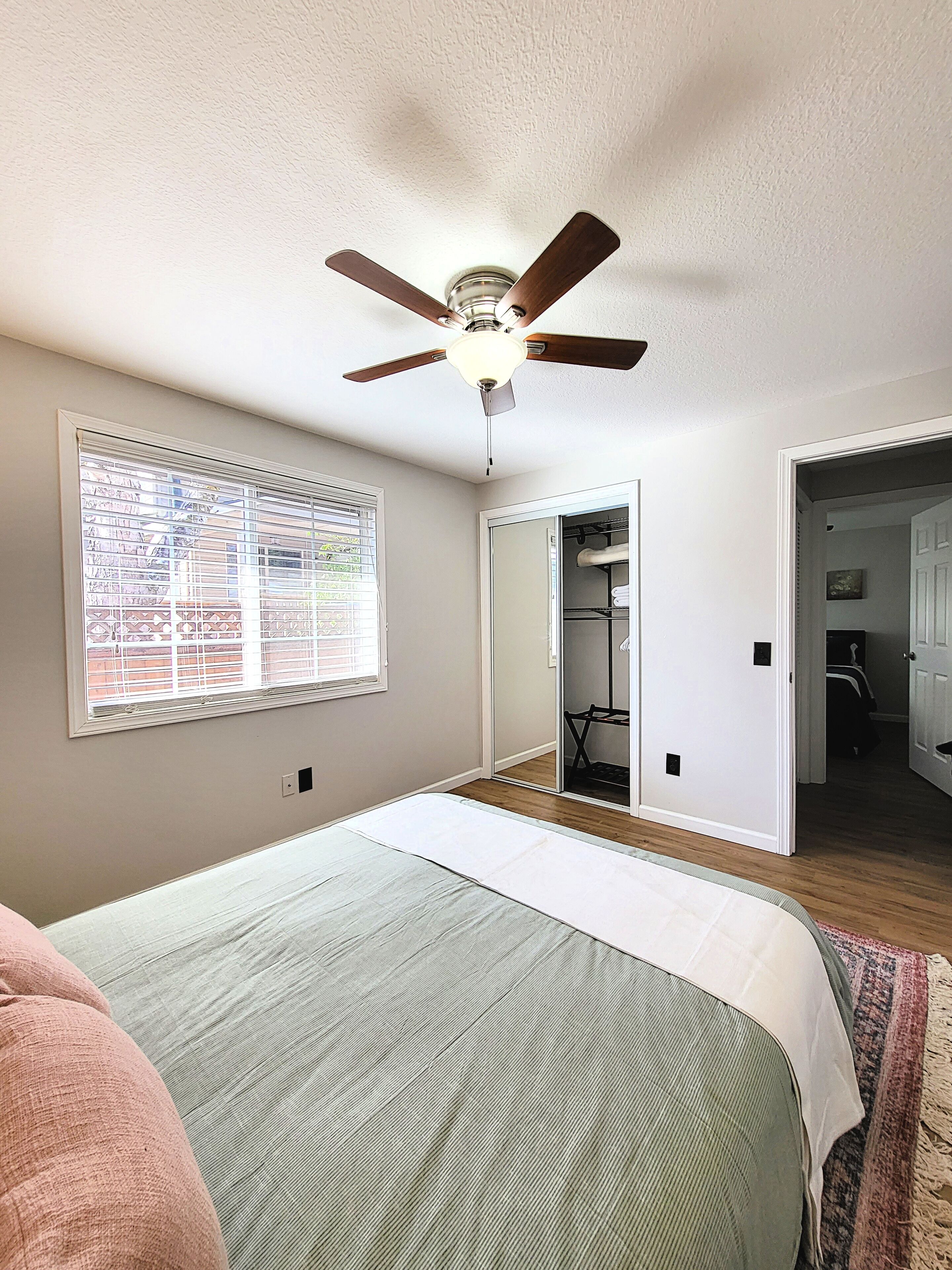Une chambre à coucher comprenant un lit, un ventilateur de plafond, une fenêtre avec des stores et un placard.