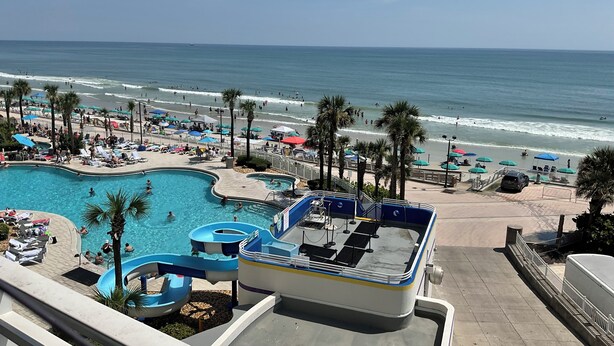 Ein Resort mit großem Schwimmbad, Wasserrutsche und Strandbereich mit Sonnenschirmen.