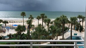 Blick auf einen Strand mit Palmen, einem Pool und Strandbereich mit Sonnenschirmen und Liegestühlen.