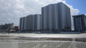 Ein Hotel direkt am Strand, bestehend aus mehreren hohen Gebäuden, einem Sandstrand und einem klaren Himmel.