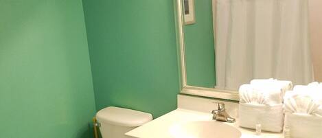 Une salle de bain avec des toilettes, un lavabo et un miroir. On trouve des serviettes et des articles de toilette sur le comptoir du lavabo.