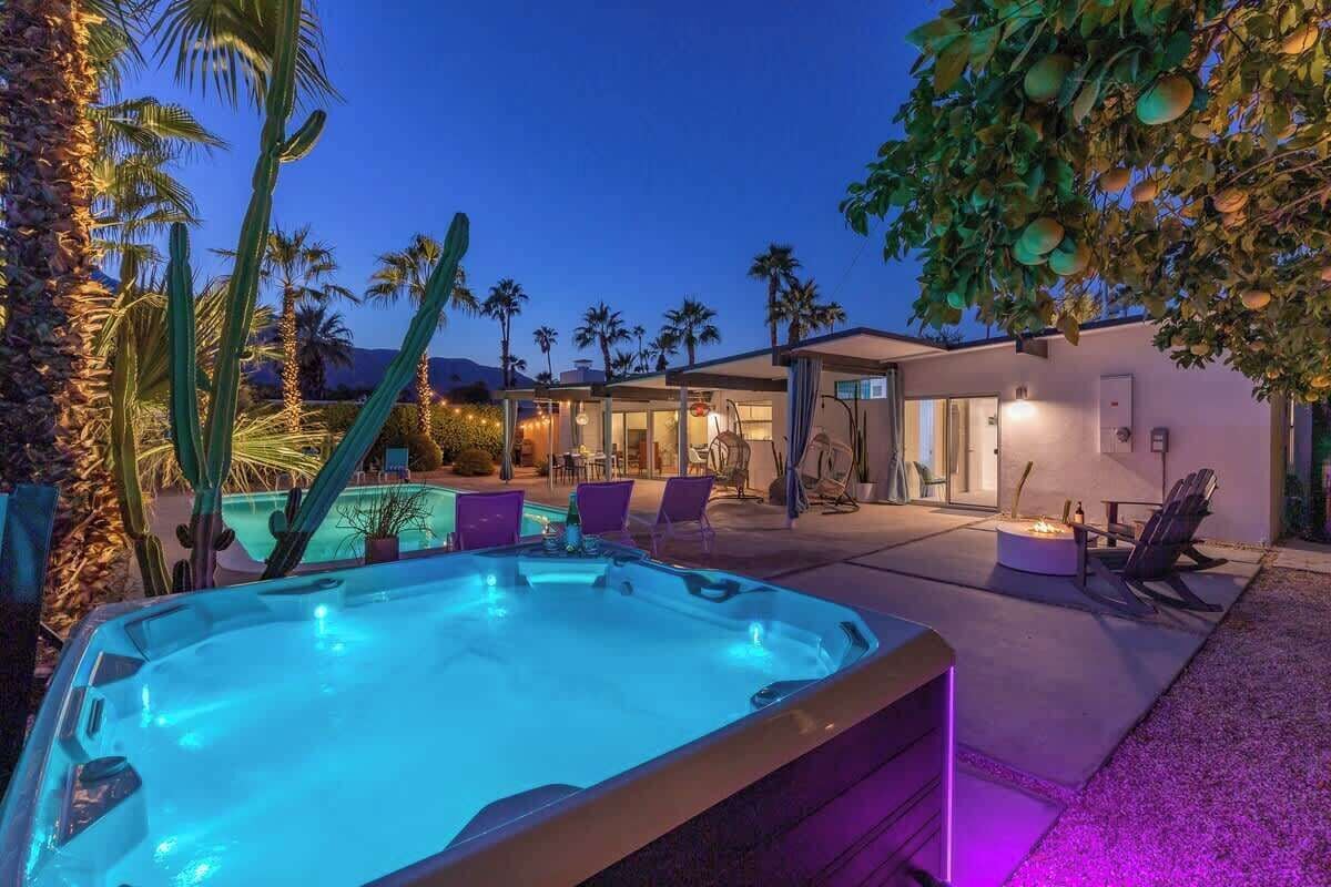 A hot tub in a backyard with a pool, palm trees, and a modern house.