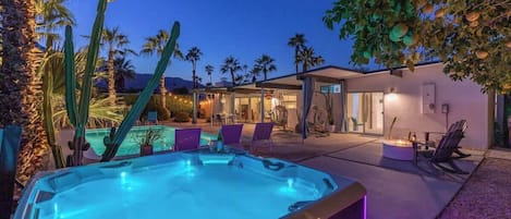 A hot tub in a backyard with a pool, palm trees, and a modern house.