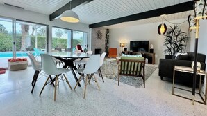 Uma sala de estar moderna com área de jantar, grandes janelas e vista para a piscina.