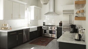 A modern kitchen with white cabinetry, stainless steel appliances, and a marble countertop.