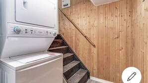 Een wasserette met een wasmachine en droger, houten trap en een houten wand.