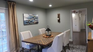 A dining area with a wooden table and white chairs, a painting on the wall, and a window with curtains. - Charming 3 BR, 2 Bath cabin located in quiet Clifftops and close to Sewanee (Monteagle)