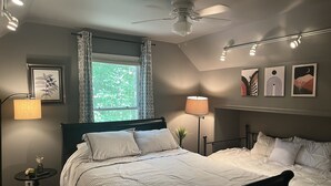 A bedroom with a bed, a ceiling fan, a window with curtains, a bedside table with a lamp, and wall art. - Charming 3 BR, 2 Bath cabin located in quiet Clifftops and close to Sewanee (Monteagle)