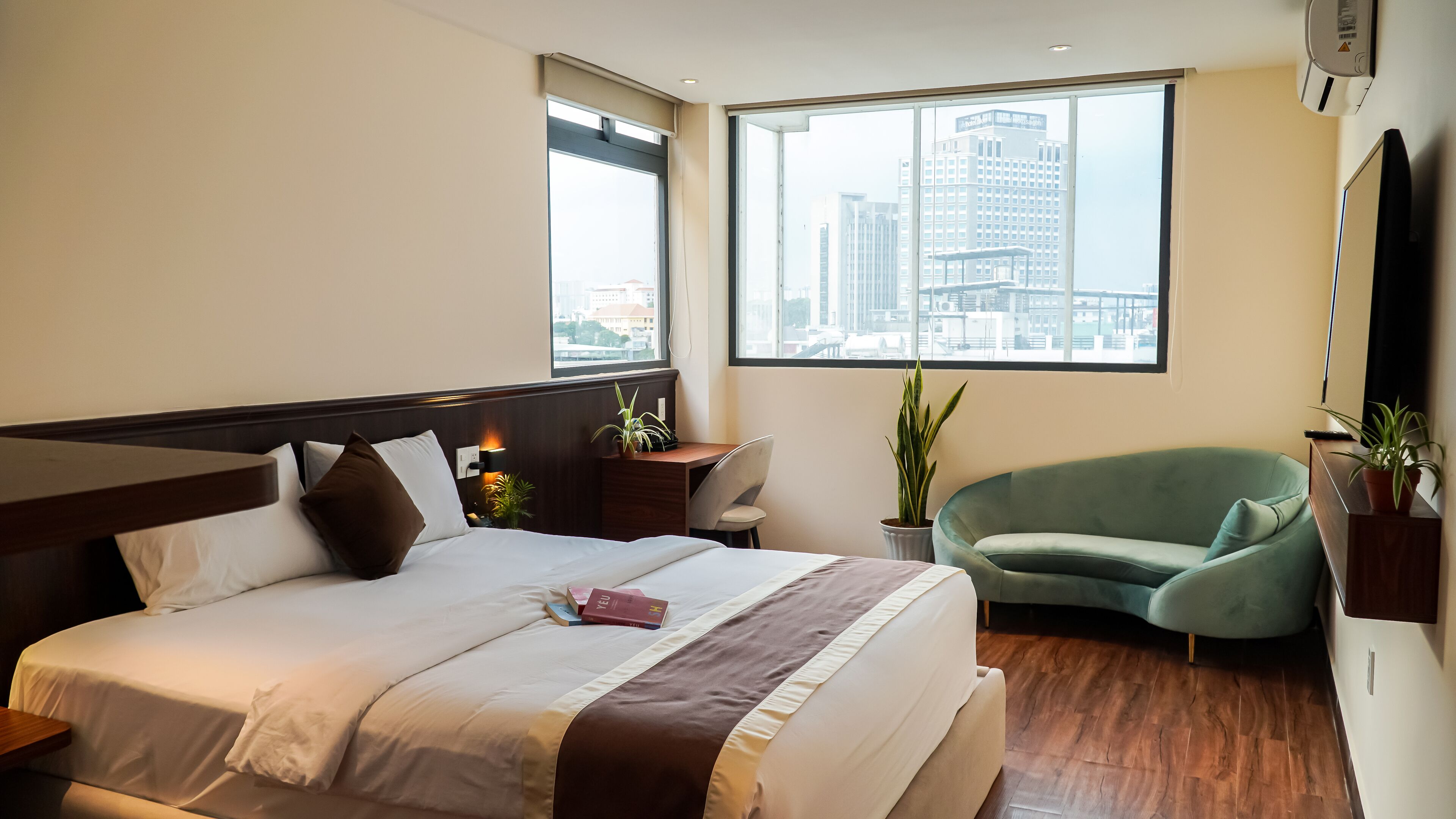 A hotel room with a large bed, a desk, a chair, and a view of the city through the window.