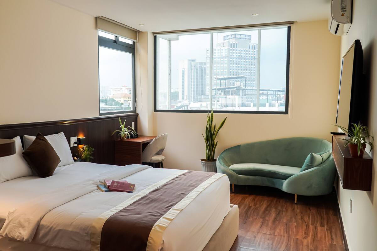 Quarto de hotel com uma cama grande, uma escrivaninha, uma cadeira e vista para a cidade pela janela.