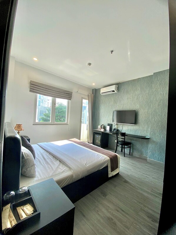 Una habitación de hotel moderna con una cama grande, un escritorio, una silla, un equipo de aire acondicionado y un televisor.