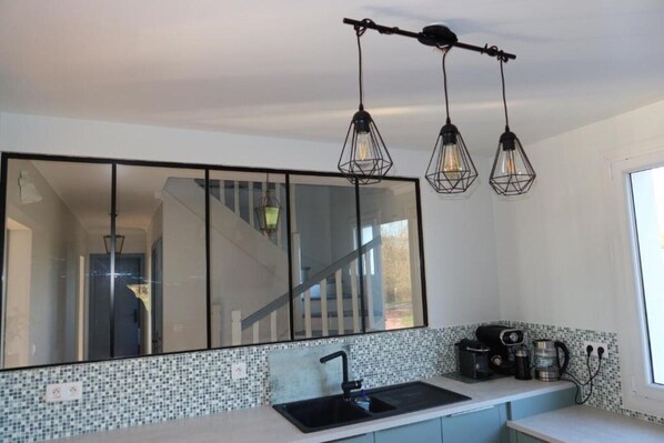 A kitchen with a large mirror, a sink, a coffee maker, and a window.
