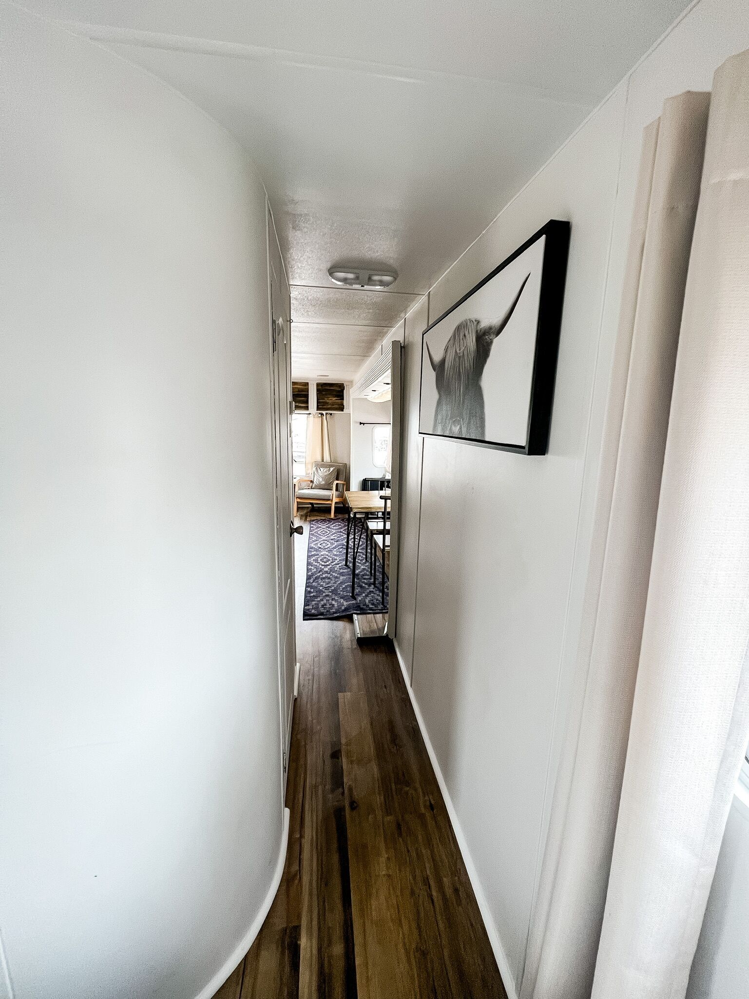 A narrow hallway with wooden flooring, white walls, and a framed picture on the right.