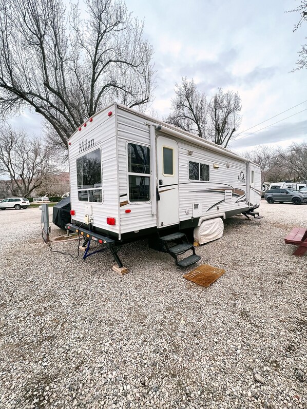 A mobile home with a ramp for accessibility, a covered area, and a gravel ground. - RustiCamper Near St. George and Zion (Leeds)