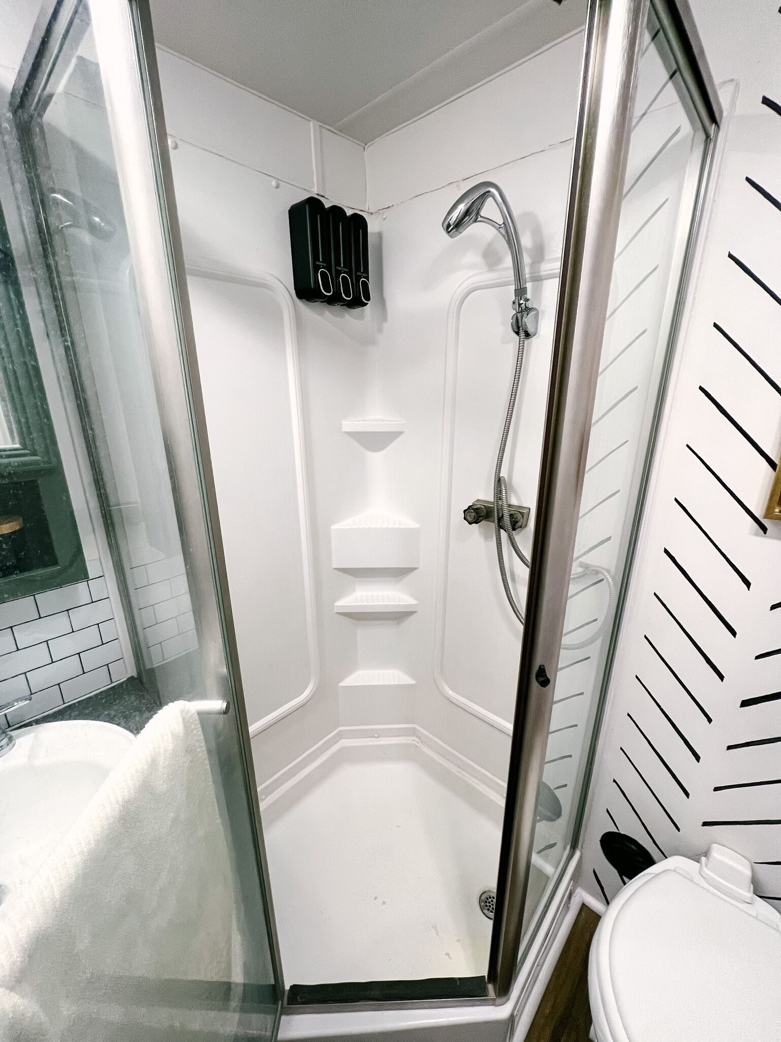 Une douche fermée par des parois en verre, dotée d’un pommeau de douche à main et d’un robinet mural.
