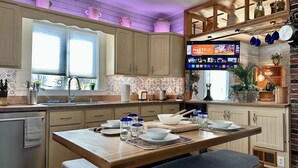 Una cocina moderna con armarios de madera, una isla central con asientos, televisor integrado y una pared decorativa de ladrillo.