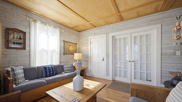 Una sala de estar acogedora con techo de madera, un sofá, una mesa de centro y una puerta con paneles de vidrio.