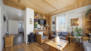 Una sala de estar acogedora con muebles de madera, un televisor y una zona de cocina con estanterías de madera.