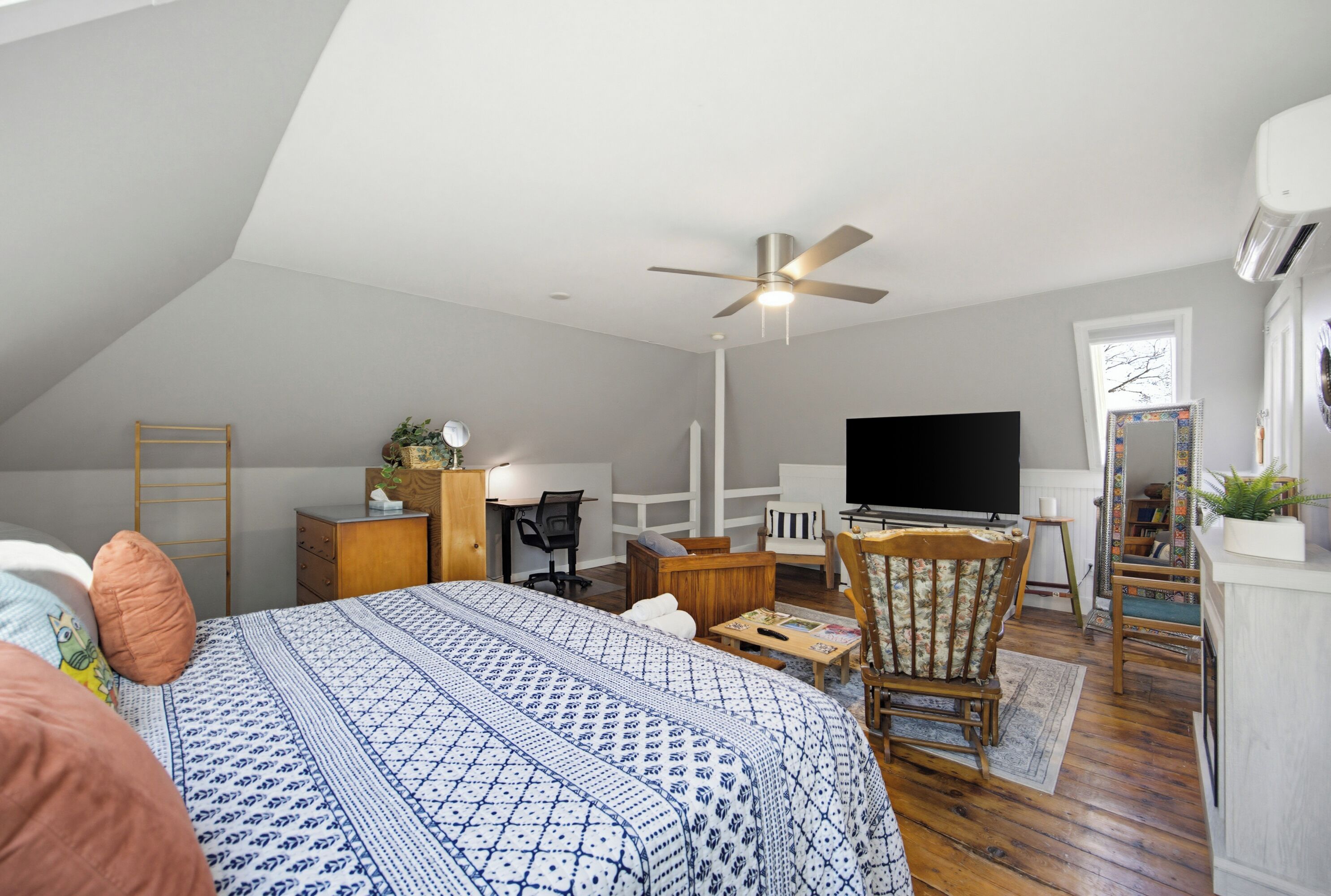 A bedroom with a bed, a desk, a chair, a television, and a ceiling fan.