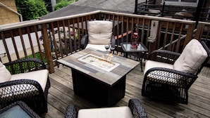 A wooden deck with wicker furniture, a fire pit, and a glass table. - Chicago Oasis | Spa Bath, Patio & Fireplace (Chicago)