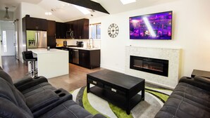 A modern living room with a fireplace, a television mounted on the wall, and a kitchen in the background. - Chicago Oasis | Spa Bath, Patio & Fireplace (Chicago)