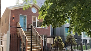 A two-story house with a brick exterior, a blue door, and a staircase leading to the second floor. - Chicago Oasis | Spa Bath, Patio & Fireplace (Chicago)