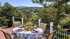 An outdoor dining area with a table set for two, surrounded by wicker chairs, overlooking a mountainous landscape. -  Cozy Chalet Retreat in Banning, California Pets-Friendly! (Banning)