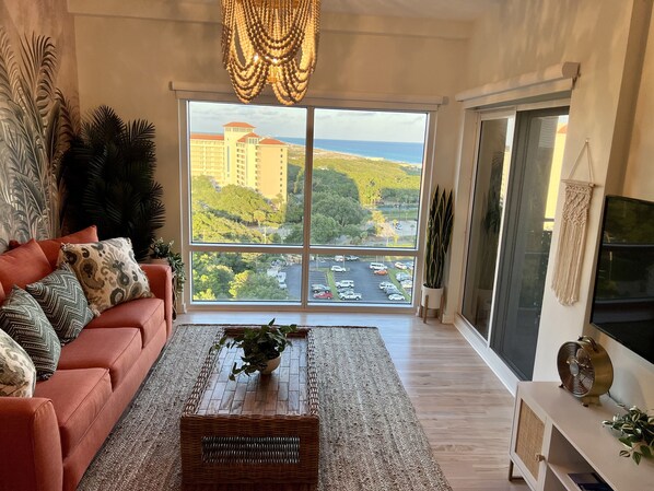 Ein geräumiges Wohnzimmer mit großem Fenster und Blick auf Stadtlandschaft und Parkplatz.