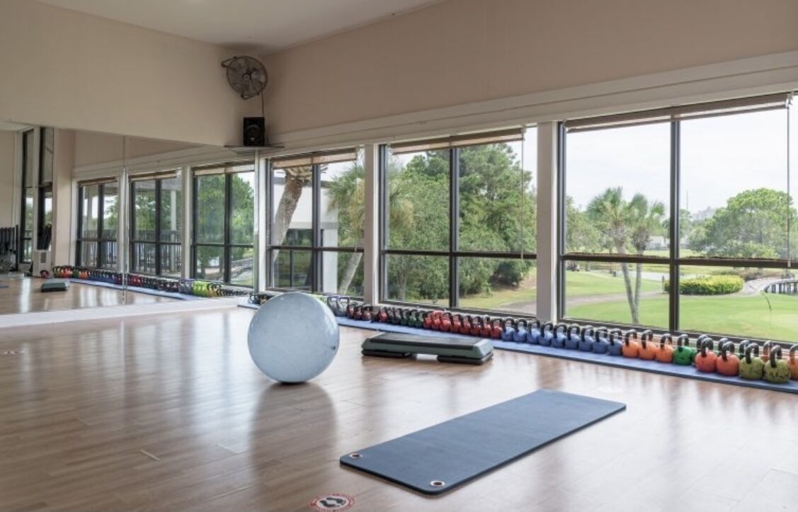 Ein großzügiger Fitnessraum mit großen Fenstern, verschiedenen Gewichten und einer Yogamatte.