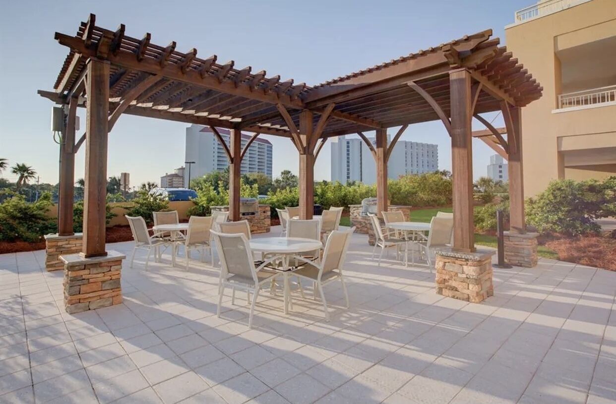 An outdoor patio with a pergola, stone pillars, and white outdoor furniture.